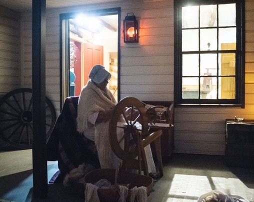 woman dressed in colonial attire at spinning wheel